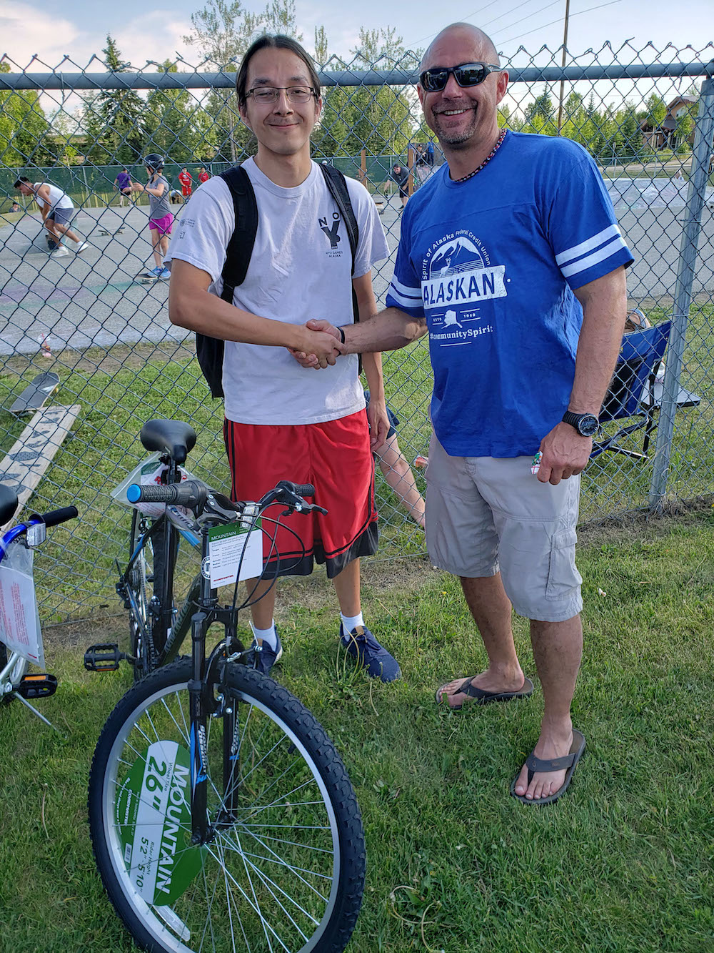 Man stands with student presenting him with a bike outside on a summer day