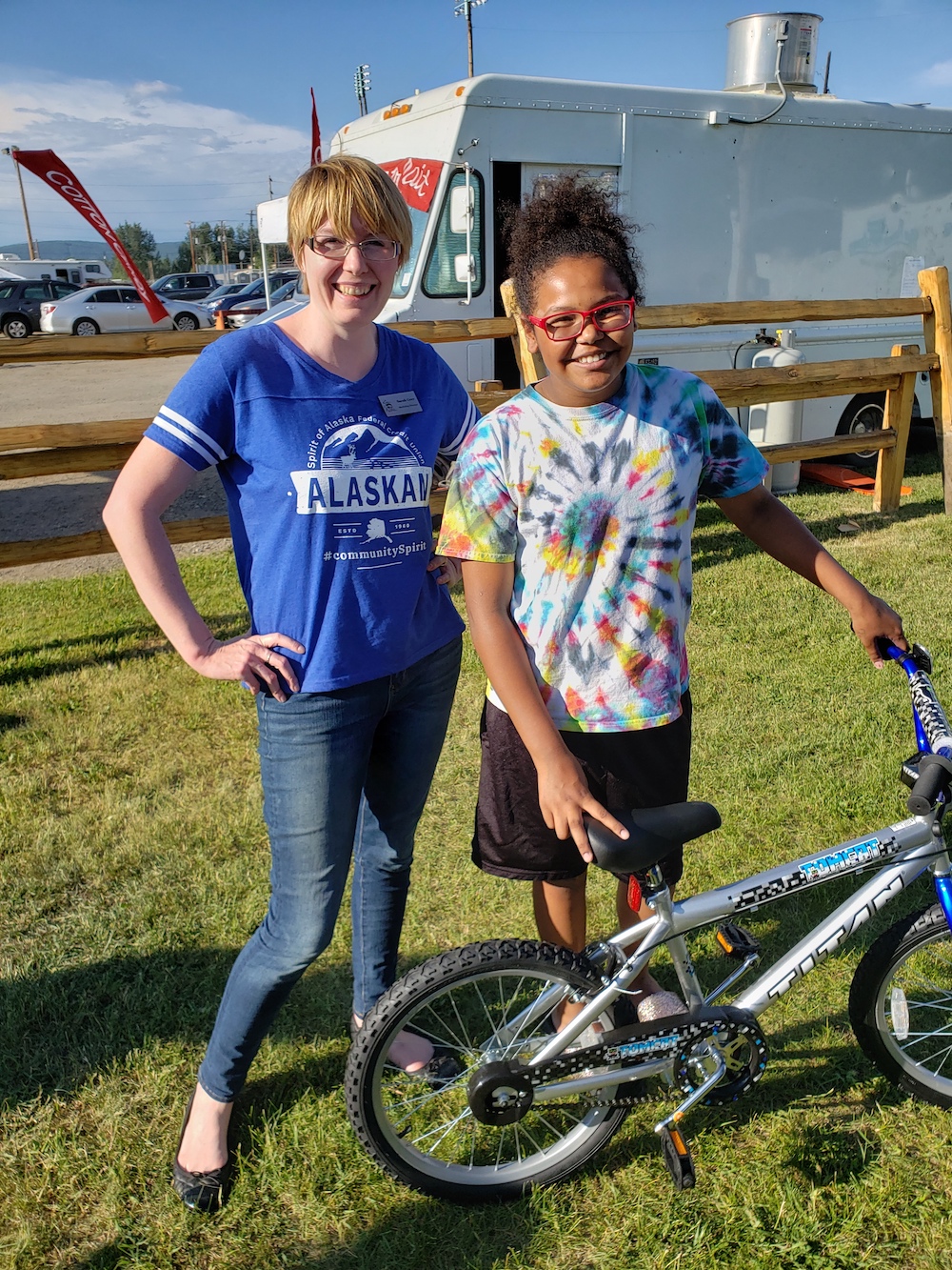 Woman stands with girl outside and gives her a silver bike