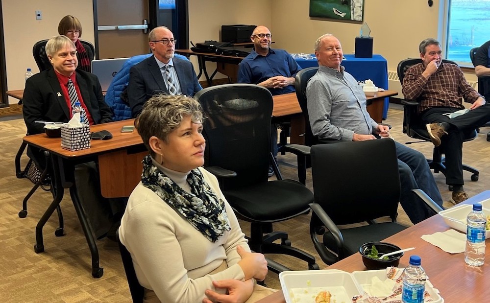 seven staff and faculty members focus during a presentation with food and bottled water