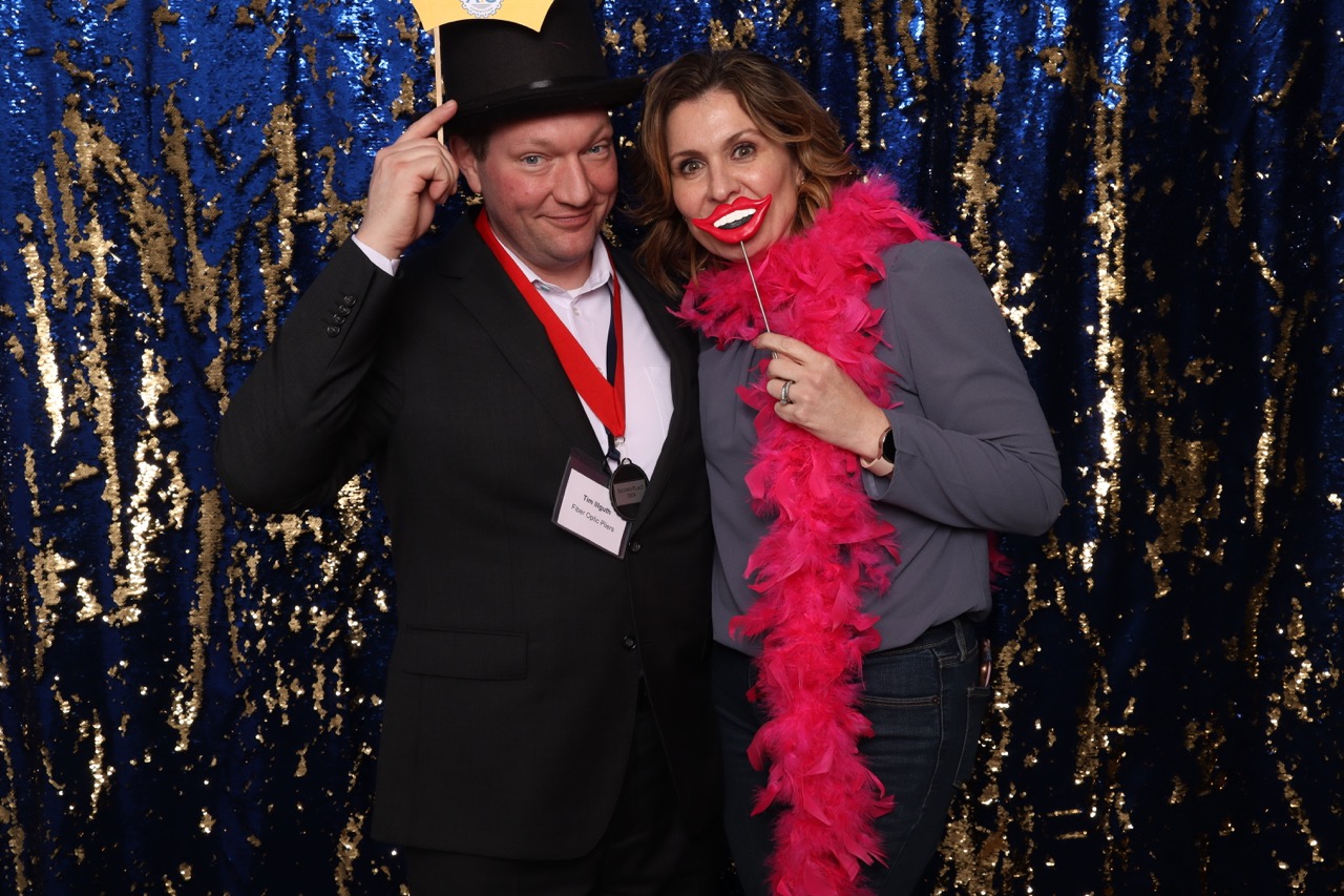 Man and woman pose together at photobooth holding props and smiling.