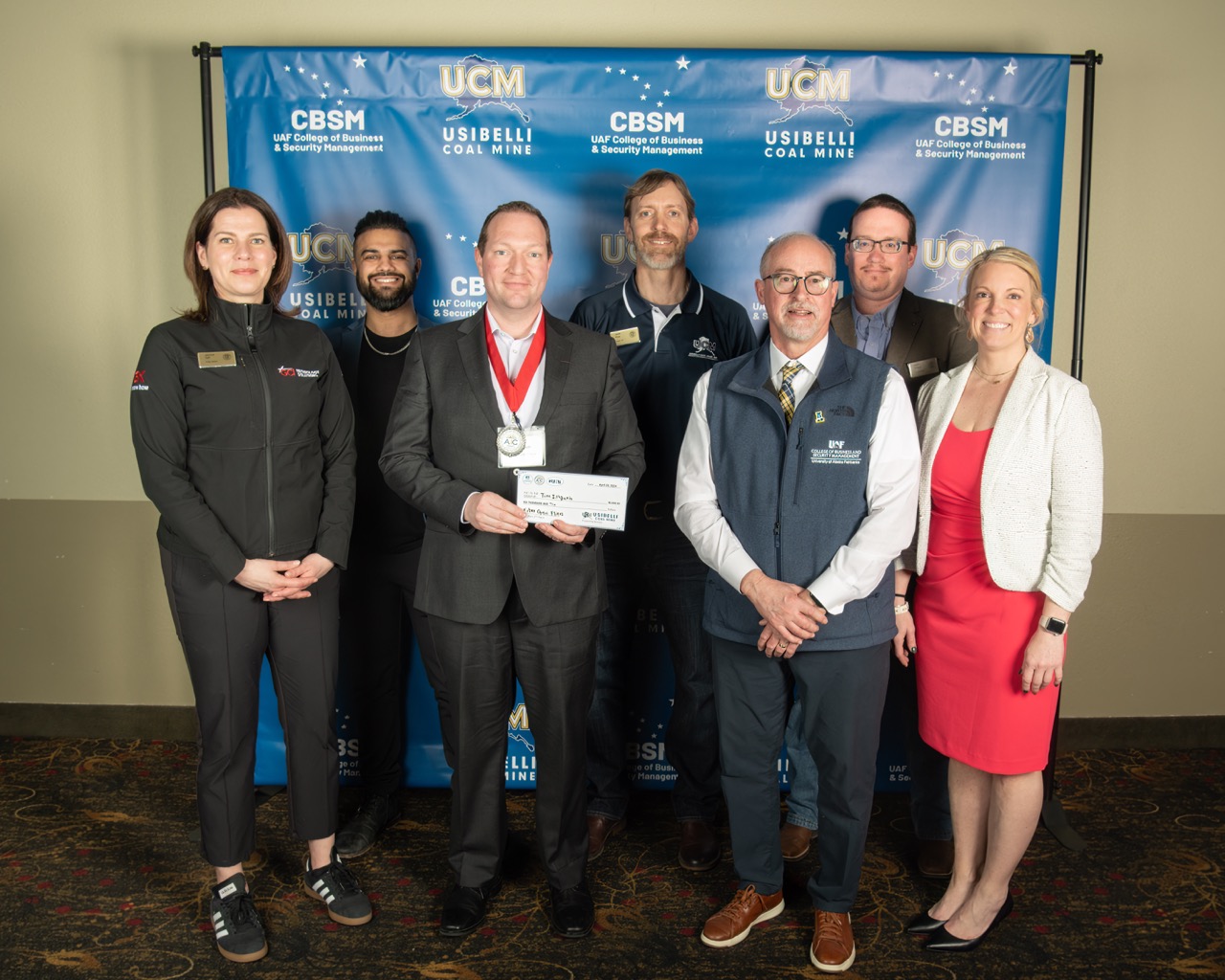 Tim Illguth holds his $6,000 prize with AIC donors, judges, and the CBSM dean.