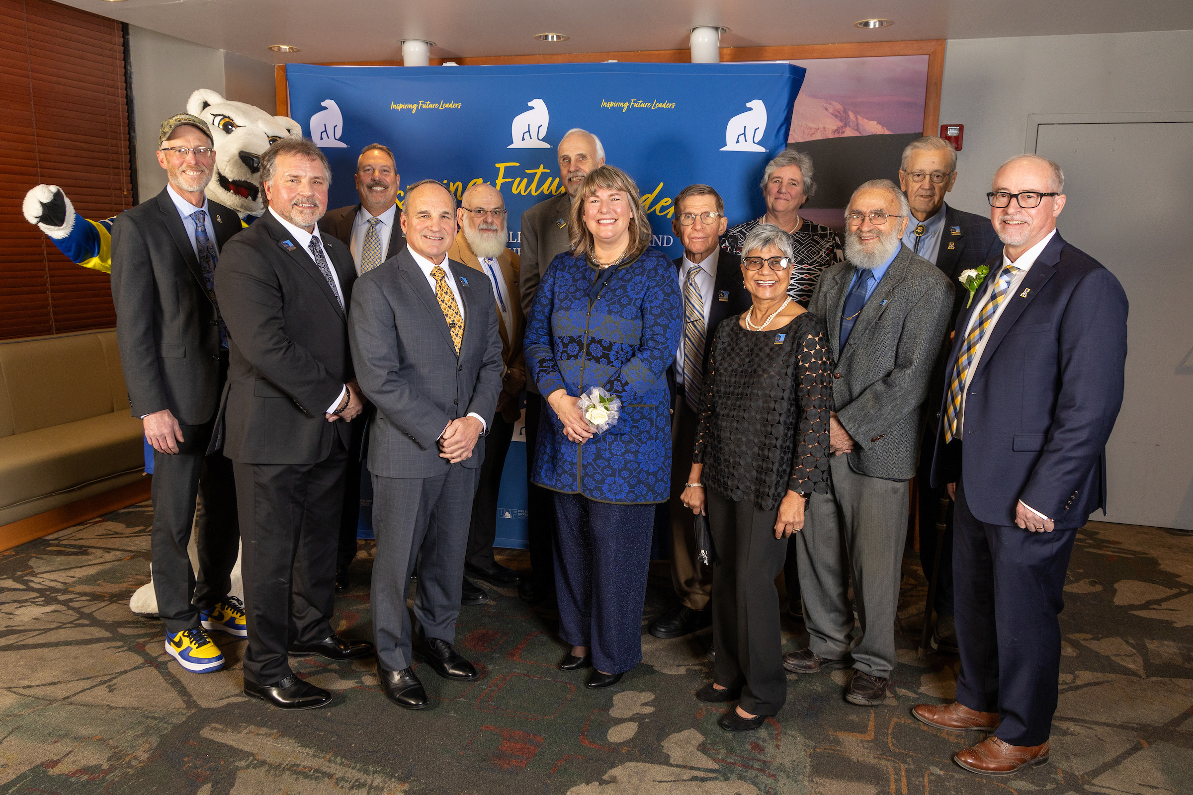 fourteen professionals in business attire stand together in front of blue and yellow photobooth with polarbear mascot