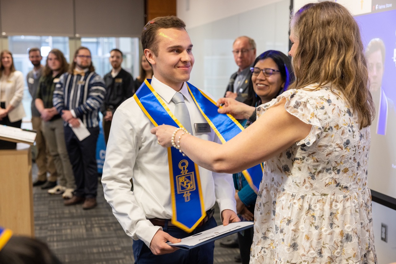 student receives blue and gold regalia from teacher