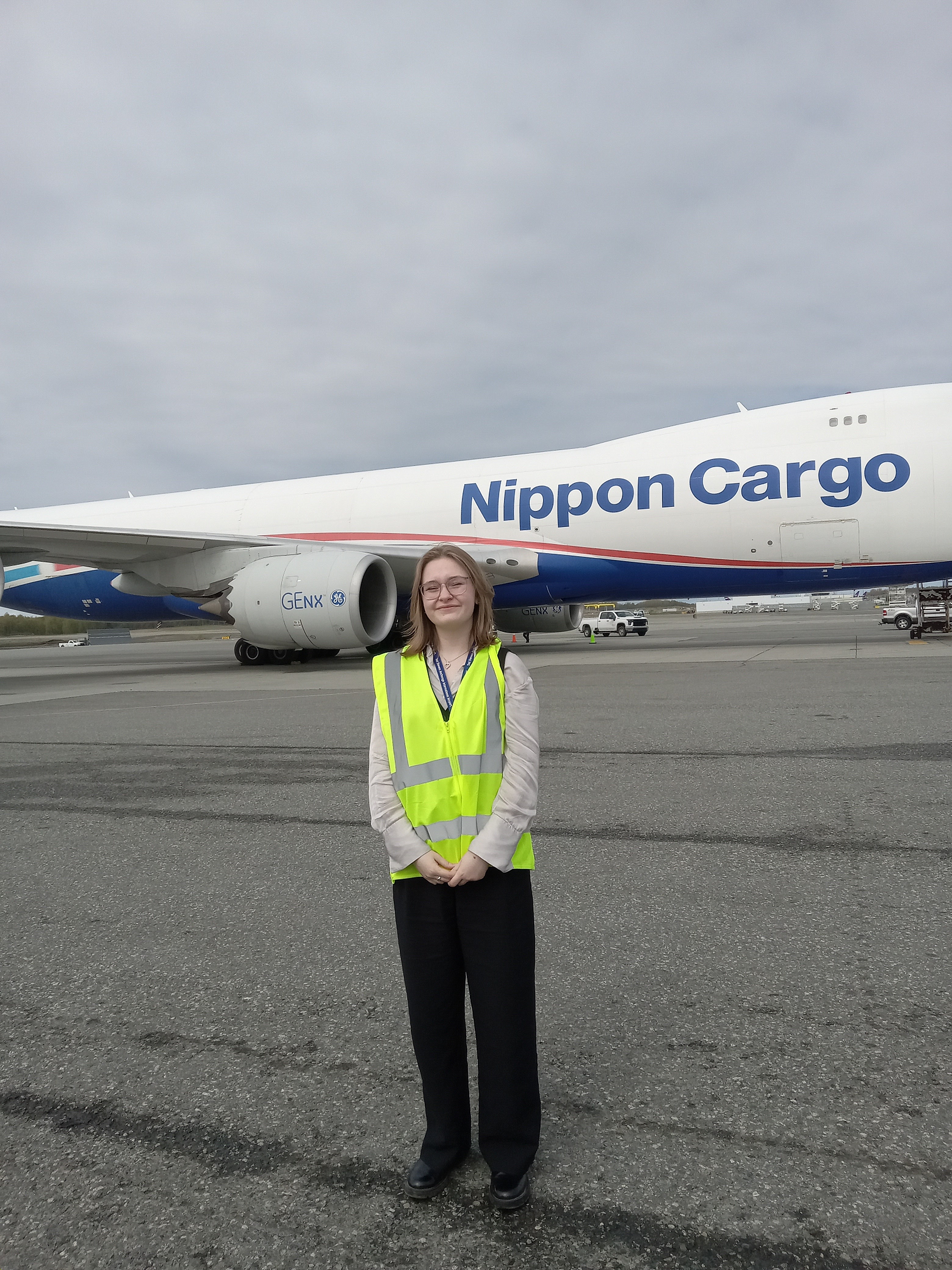 Student in yellow hardhat standing atop pallets in front of backdrop of fall colored hills