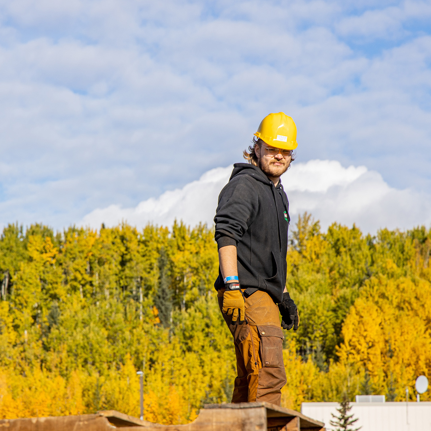 Student in yellow hardhat standing atop pallets in front of backdrop of fall colored hills