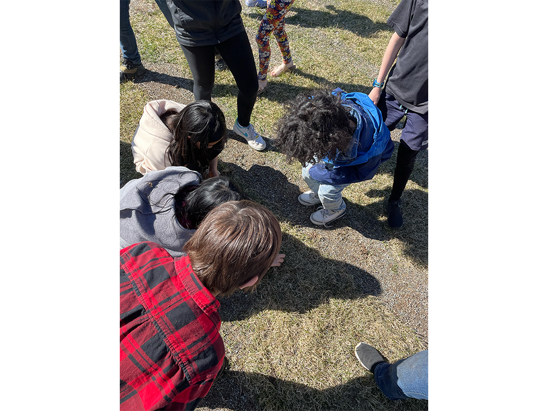 Group of kids gathered around an area on the ground