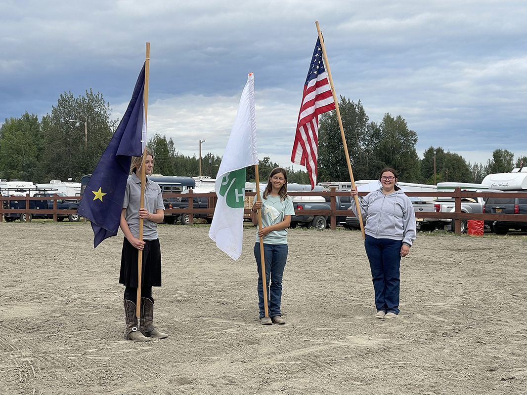 Three people holding flags in a dirt field
