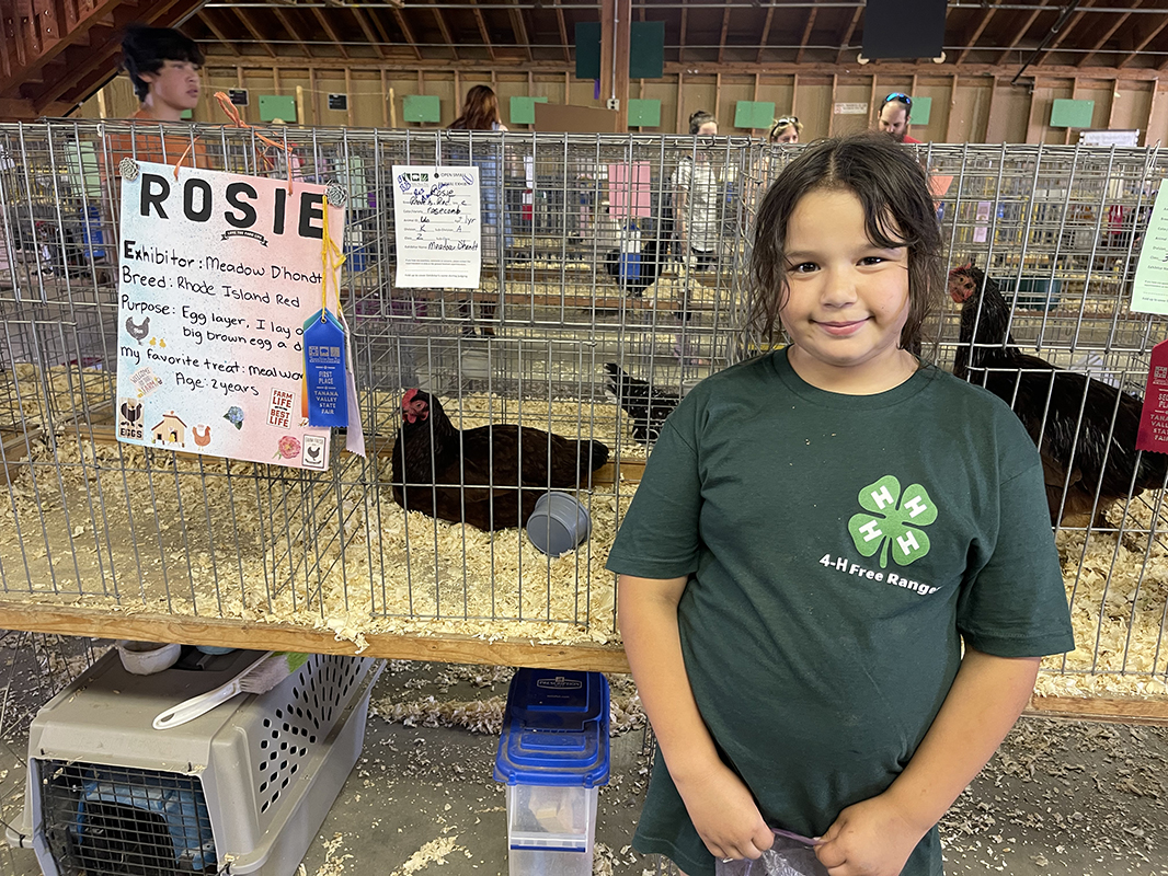 A young girl stands before a chicken cage