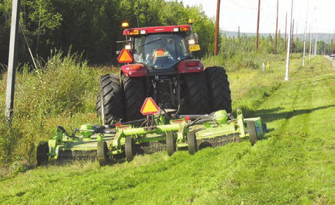 A tractor pulls a mower across a lush, green grassy field under a clear blue sky