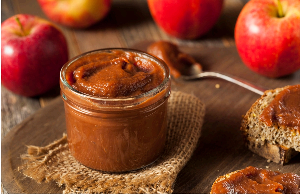 Jar of dark red spread next to red apples