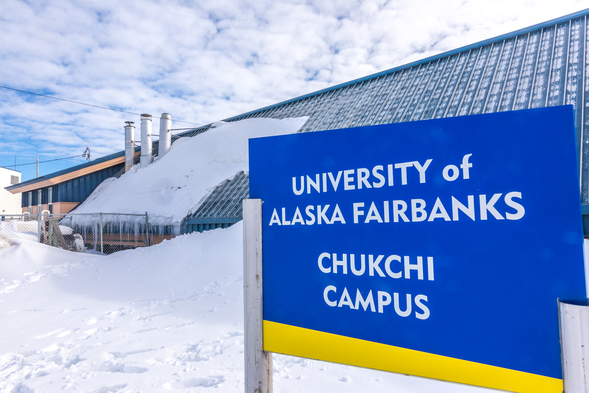 A smiling student standing outside the Chukchi Campus exterior sign