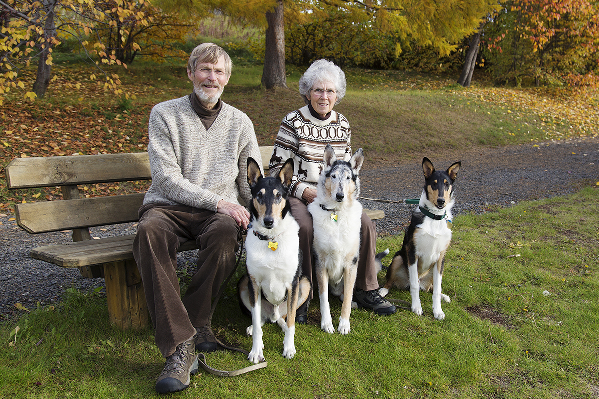 Jon and Jane Aspnes pose on a park bench with their three dogs.