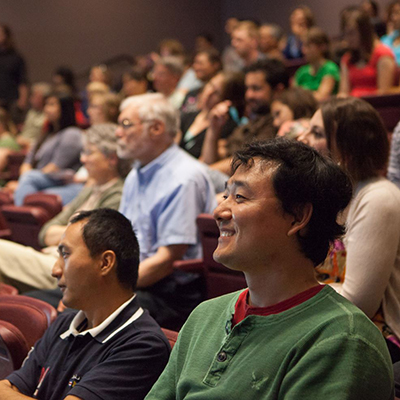 An full auditorium smiles as they listen intently to an off-camera speaker.