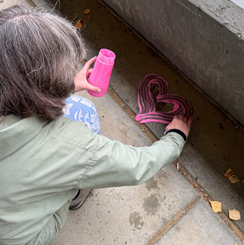 Women, Gender and Sexuality Studies program coordinator Carol Gray draws a heart with pink washable chalk paint on a concrete walkway of the UAF campus, spreading positivity for Suicide Prevention Month.