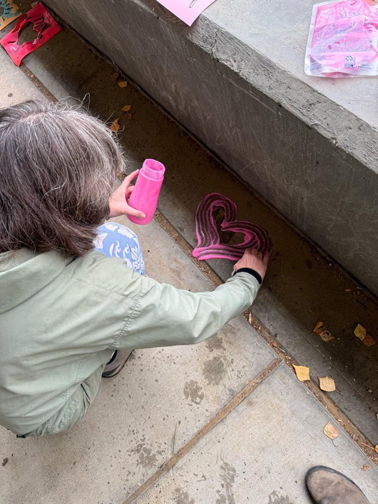 Carol Gray draws a heart with pink washable chalk on the UAF campus concrete walkway. UAF Photo by Jamie Haman