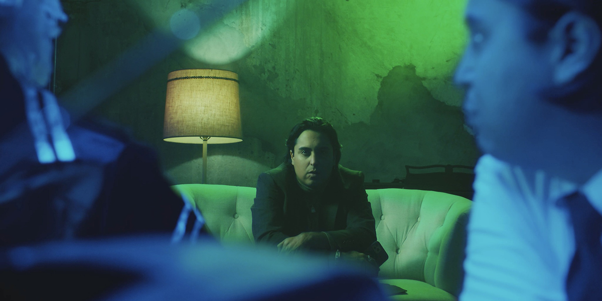 A man sits on a couch in a green room. Image courtesy of the Sundance Institute