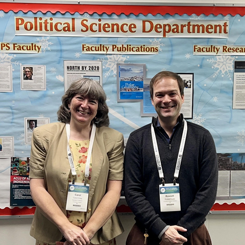 Political Science faculty Carol Gray and Russell Luke pose in front of the Political Science Department billboard