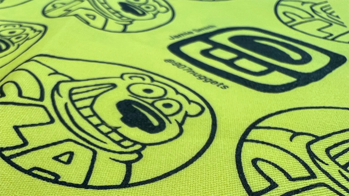 Bright yellow fabric patterned with smiling cartoon bears wearing CLA shirts in circles. UAF image.