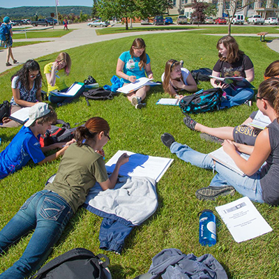 A group of students having class outdoors in the grass on a sunny afternoon