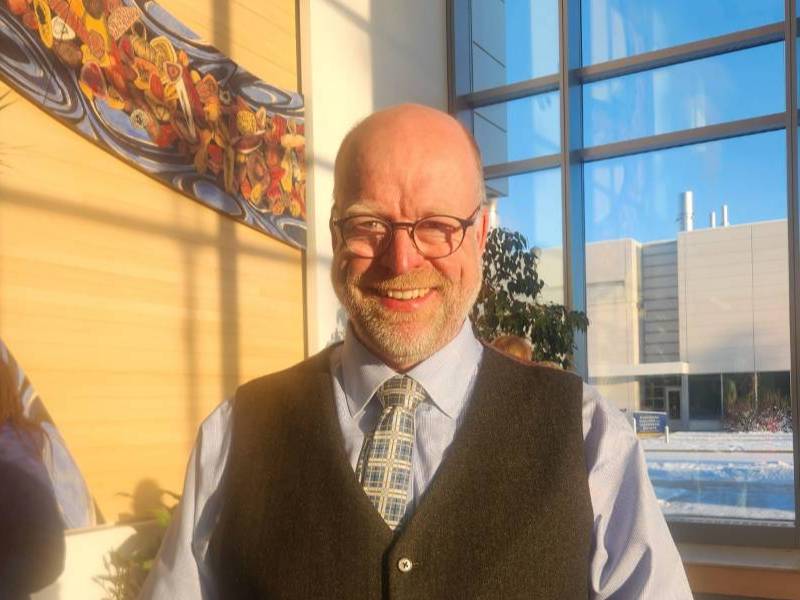 Man with glasses and vest smiling broadly in a sunny building lobby