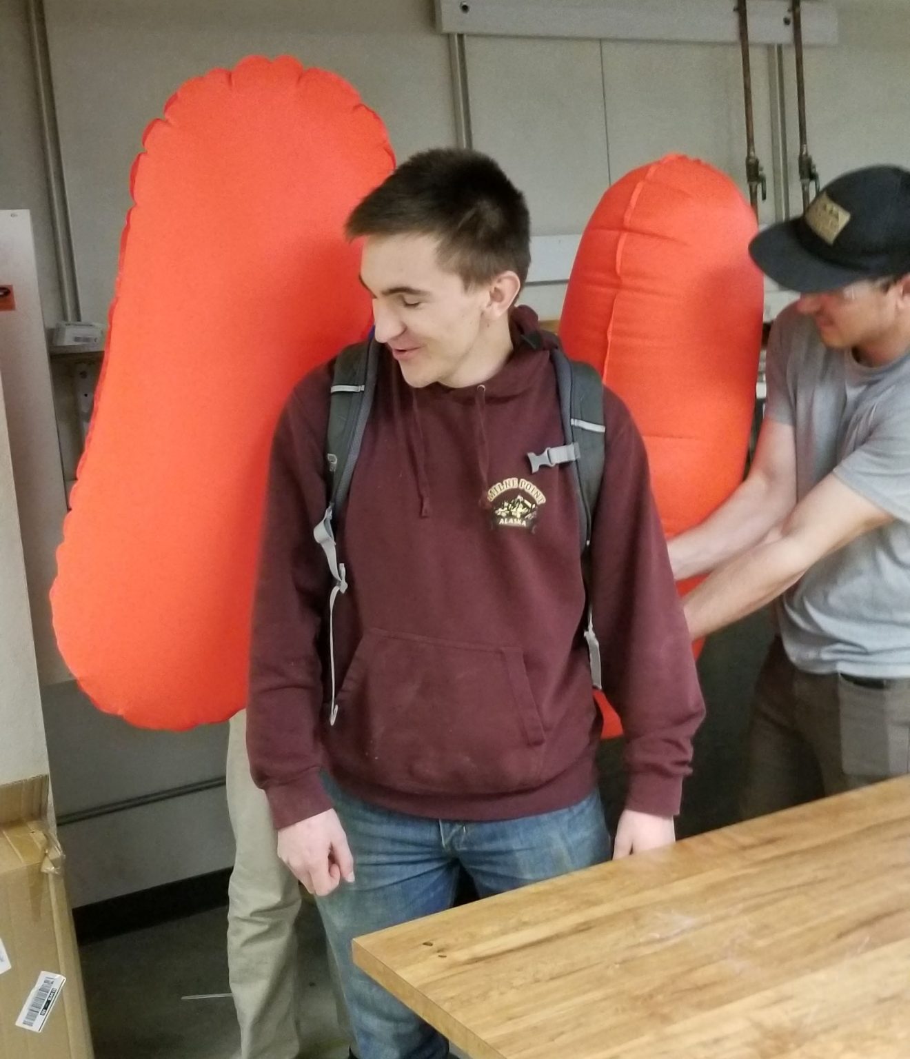 A student has two pouch-like wings attached to his back by two other students.