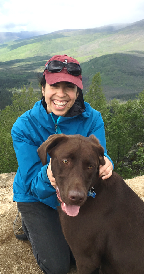 Andrea Bersamin kneels on a rock outcropping with a chocolate labrador.