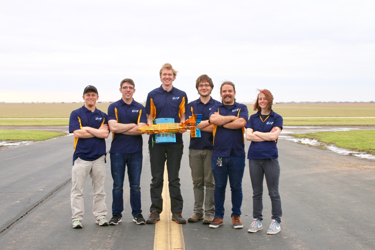 Group photo of students standing on a runway holding a drone