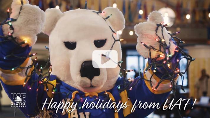 closeup of Nanook mascot holding colored tree lights with a play button overlaid; text says "happy holidays from UAF!"