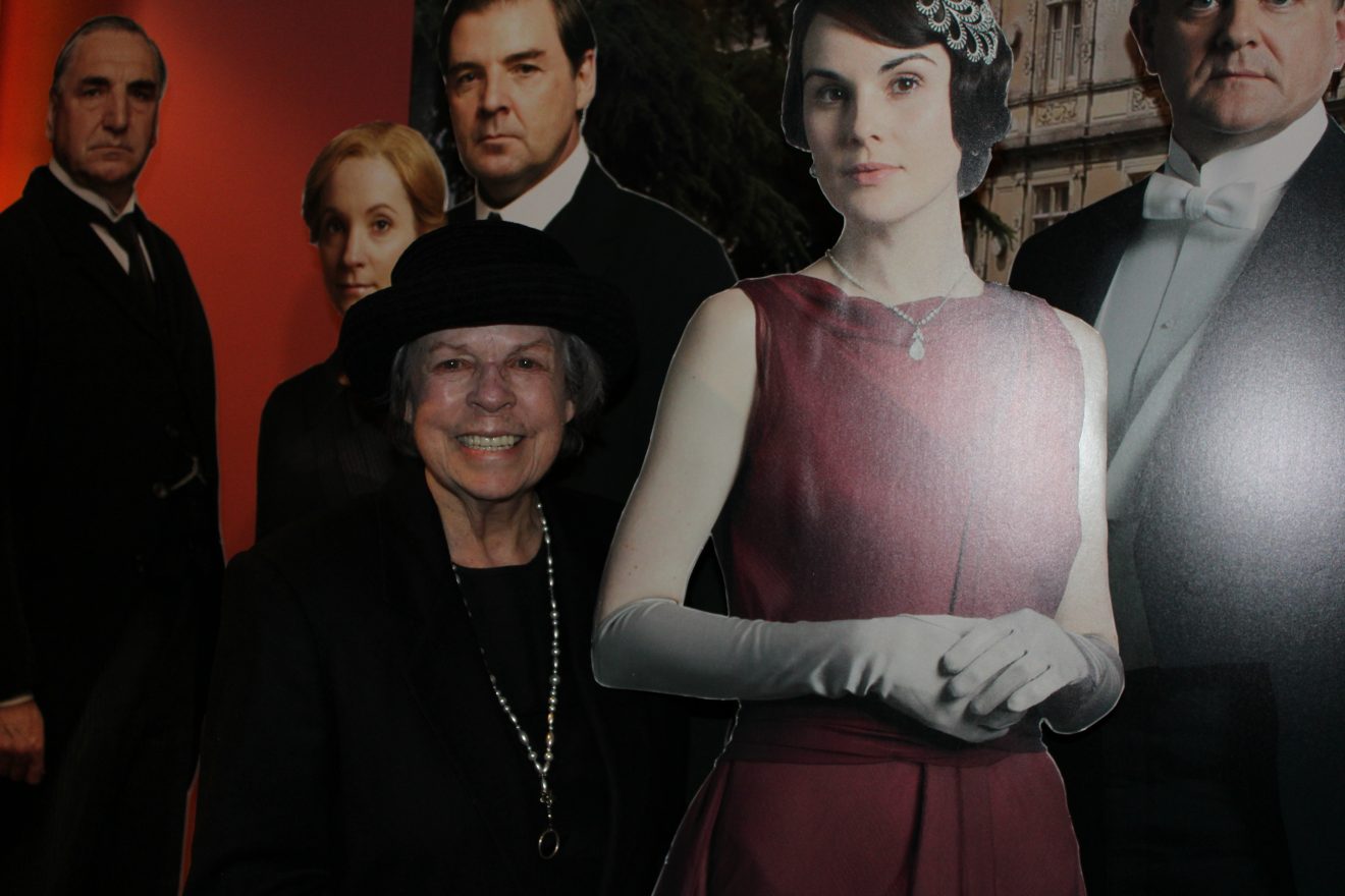 Marcella Hill dressed as housekeeper Mrs. Hughes from Downton Abbey. She stands among cutouts of other characters from the show.