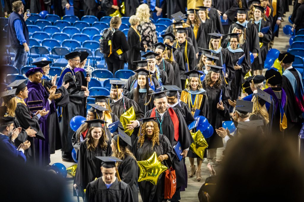 Flanking the graduates in two lines, members of the faculty congratulate the graduates during the 2019 commencement recessional at the Carlson Center.