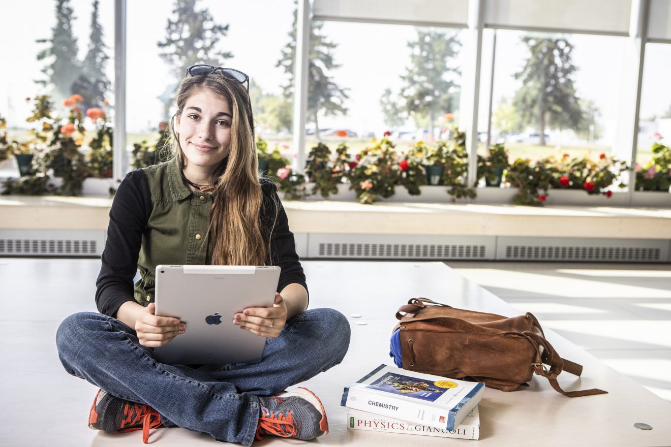 Madeline Burton holding iPad and sitting next to Chemistry and Physics books.
