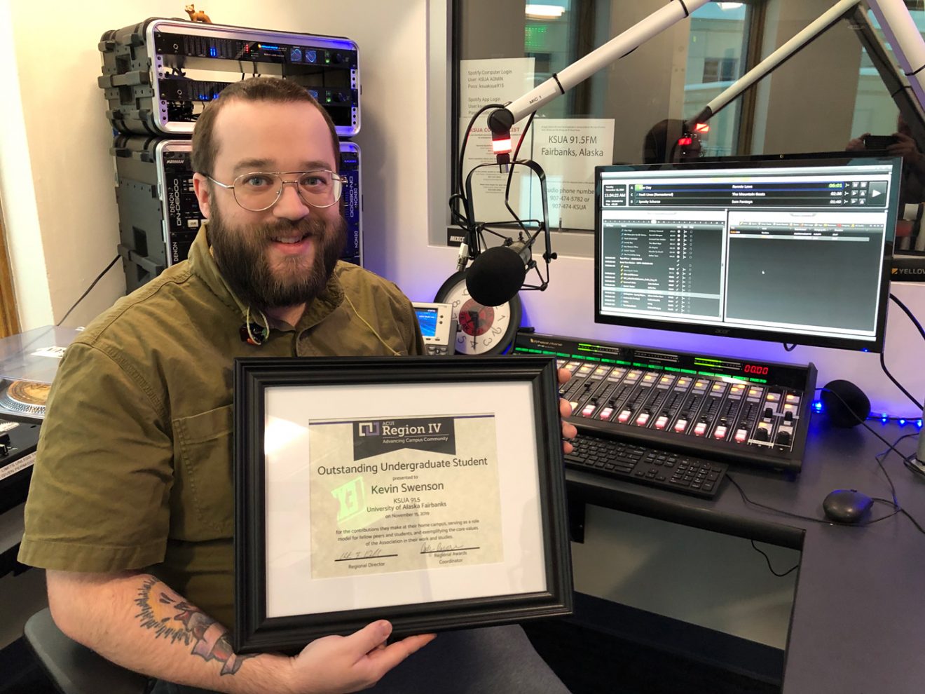 Kevin Swenson holds his framed award in the KSUA radio station.