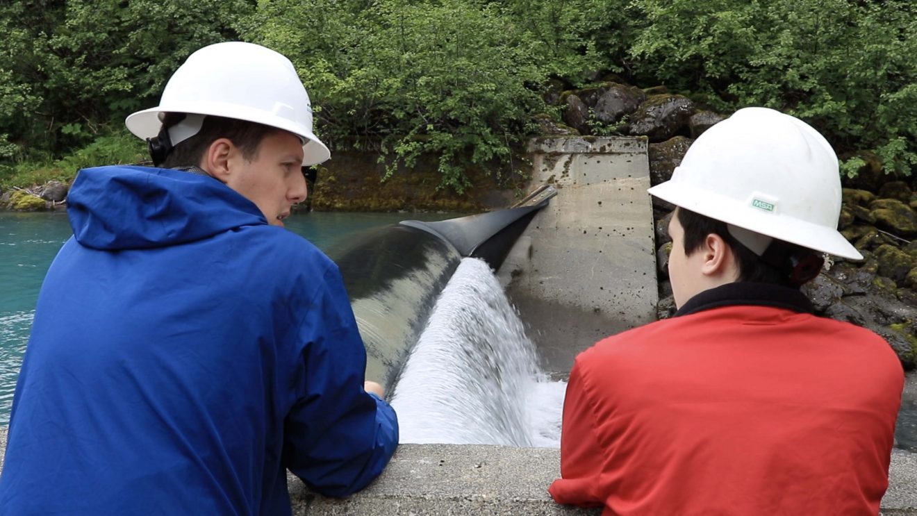 Kurt Nunn (right), a 2019 intern, talks with Cordova Electric Project Manager Craig Kuntz as water spills from the Power Creek Hydro Project.