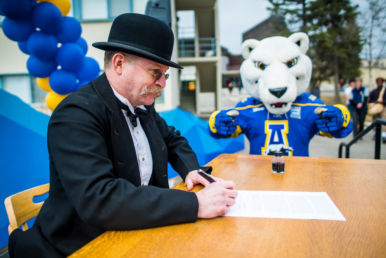 A reenactor plays the role of Gov. Strong signing the bill creating the Agricultural College and School of Mines on May 3, 1917. The Nanook mascot stands in the background.