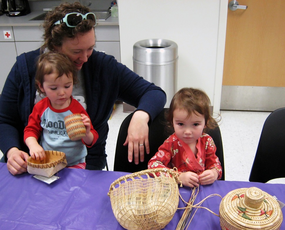 two children and one adult sitting at a table looking at woven baskets.