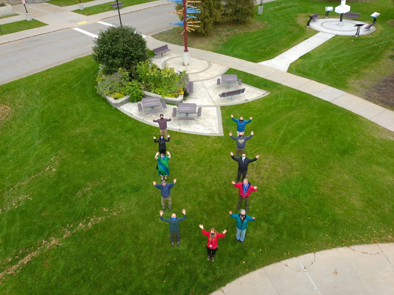 Aerial shot of a group of people standing on the grass. Their bodies form a giant "U," and their arms are also held up in a U shape.