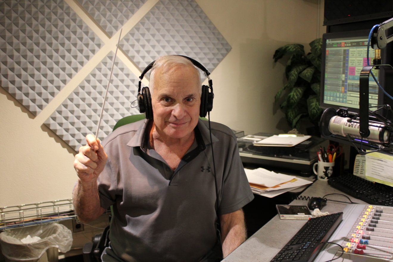 Bob Fischer with headphones and holding a baton in a radio sound studio