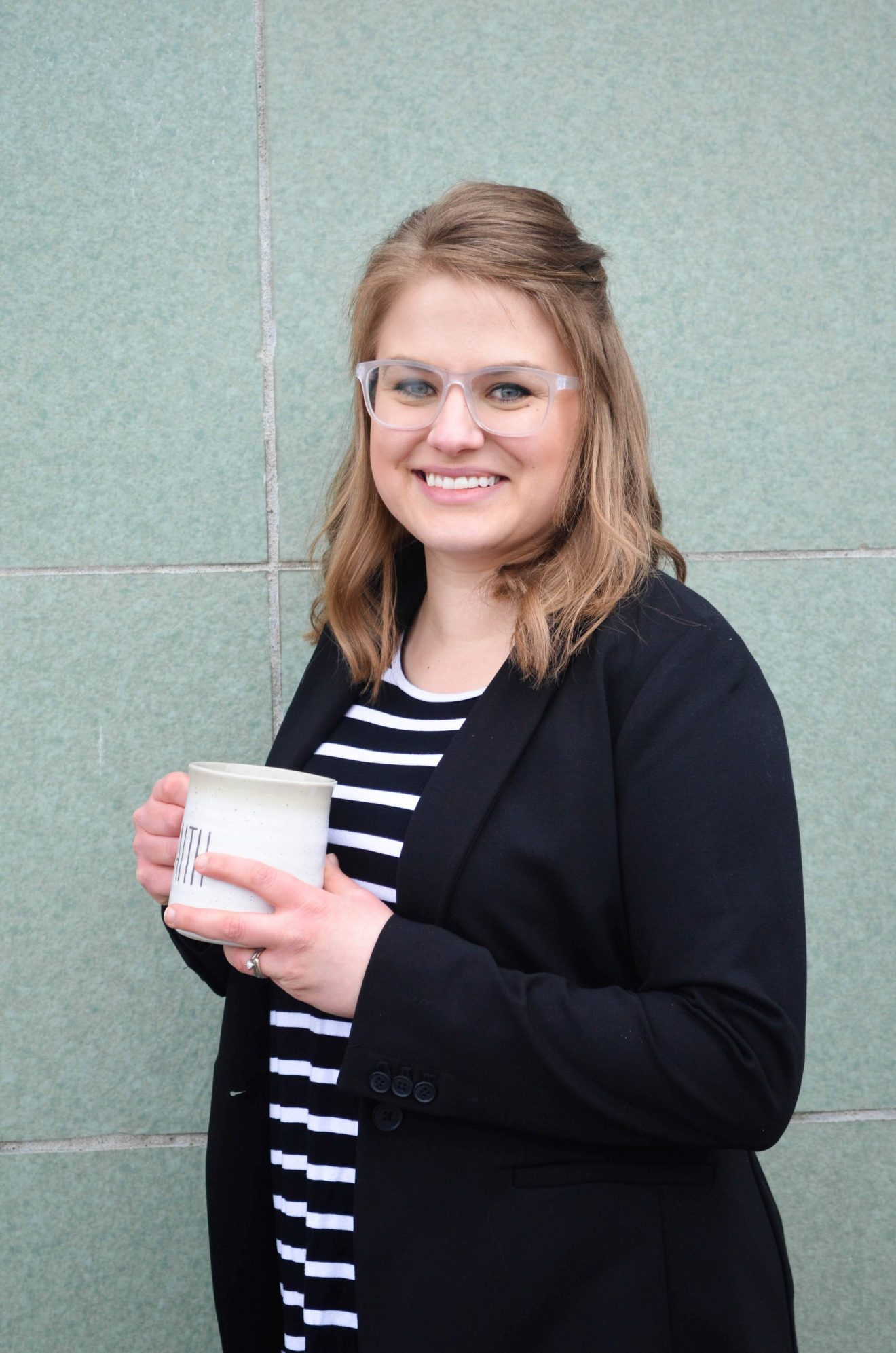 Photo of woman standing in front of a wall. She is holding a mug.