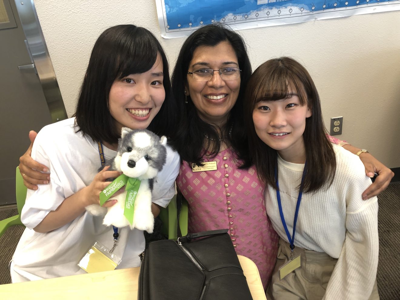 Three women poses for the camera. One is holding a small plush dog that is a souvenir.