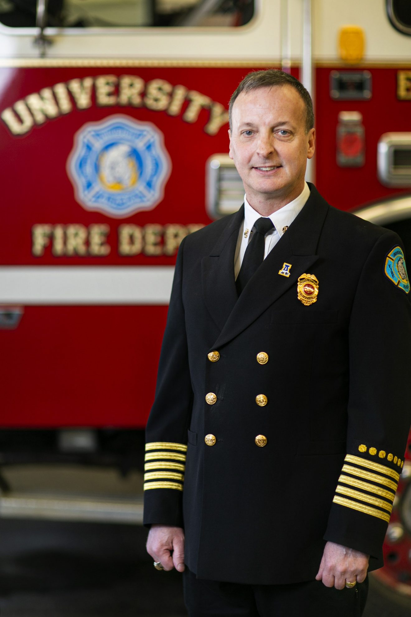 A man in dress uniform stands in front of a fire truck.