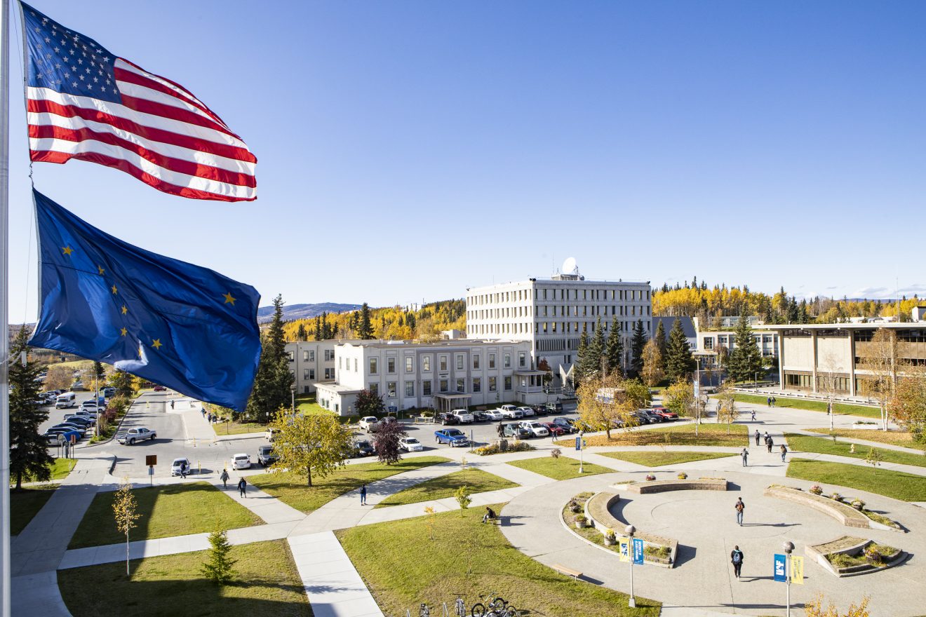 View of east side of campus on sunny fall day. The U.S. and Alaska flags are flying nearby.