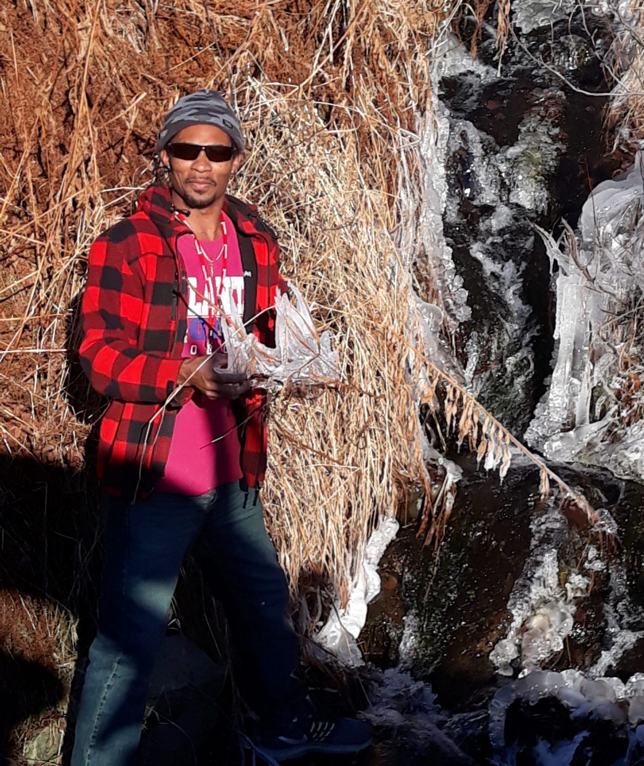 Man wearing sunglasses standing near what seems to be a frozen waterfall.