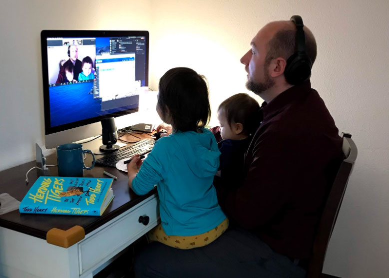 Sean Holland sitting at his computer with his two daughters on his lap.