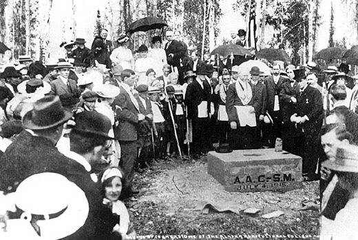 Black and white photo. Large crowd gathering around cornerstone laid in the dirt.