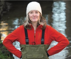 Woman wearing a hat and chest-high waders standing beside or in a body of water
