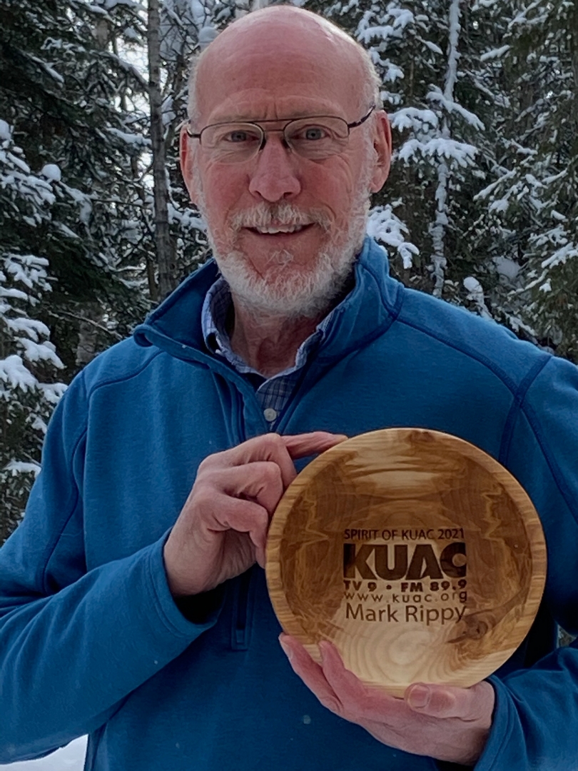 Man standing outside in winter holding a bowl with KUAC and his name written on it.