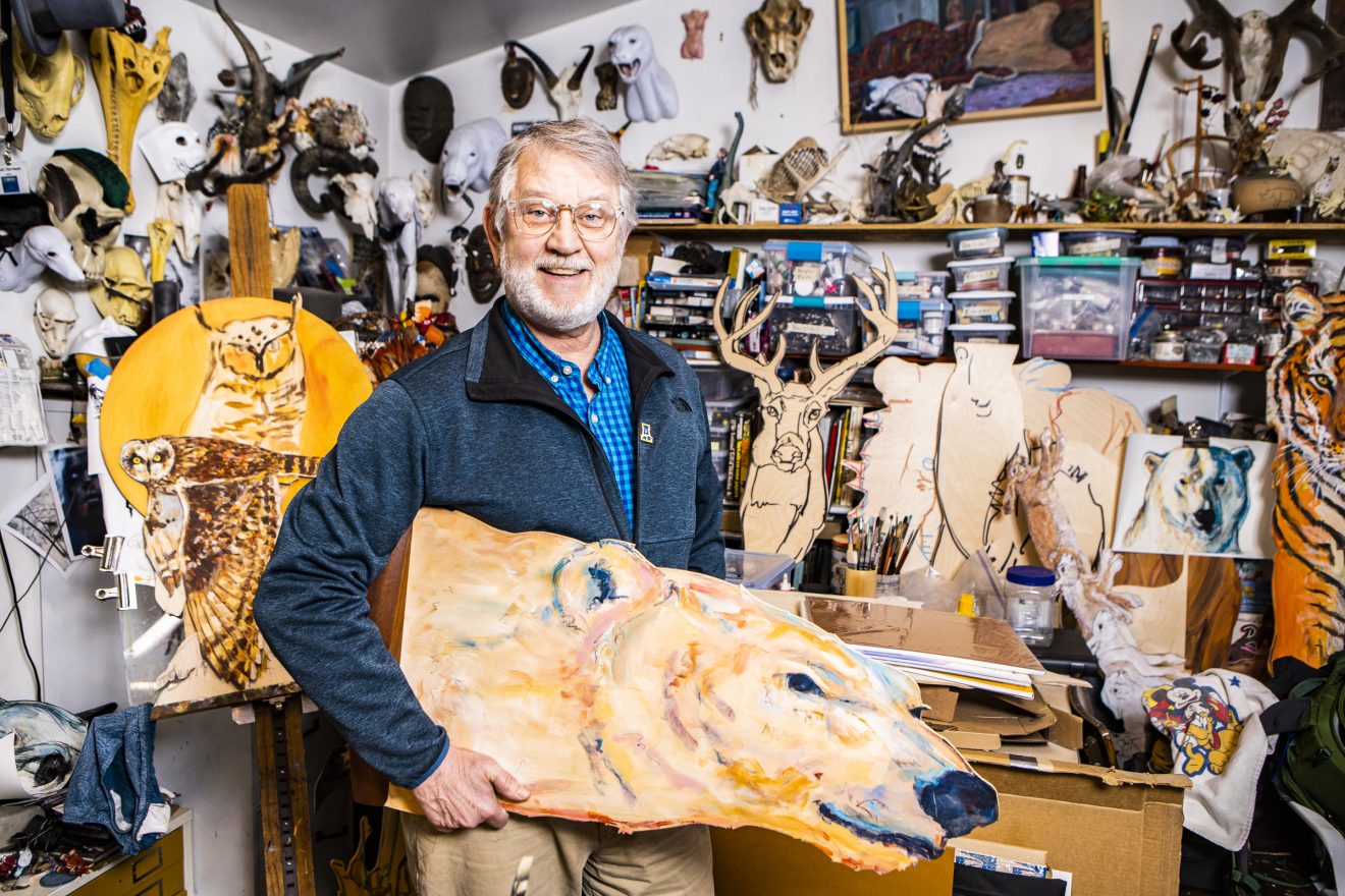 Man holding a wooden Nanook cutout and surrounded by paintings, carvings and other art