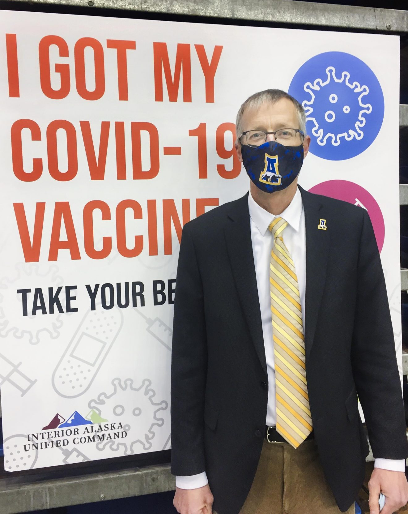 Man wearing a mask standing in front of a sign that says "I got my covid-19 vaccine"