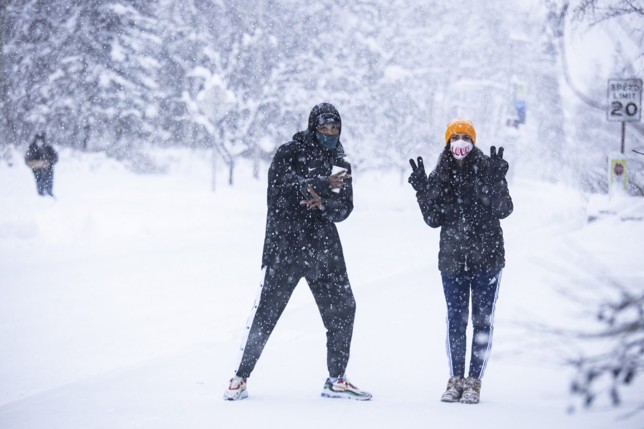 Two students sport peace signs and masks during a heavy snowfall.
