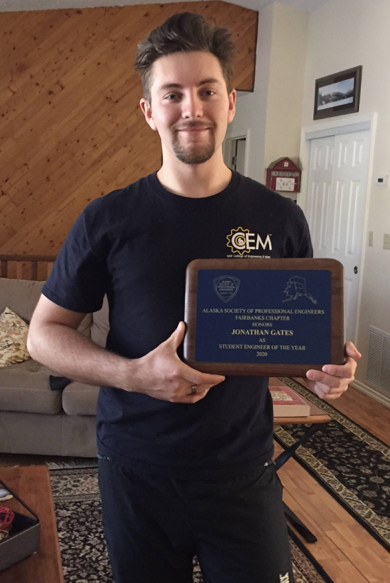 Jonathan Gates stands in a living room holding a plaque.